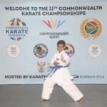 A young karate student wearing a blue belt and representing Canada poses proudly at the Commonwealth Sport event.