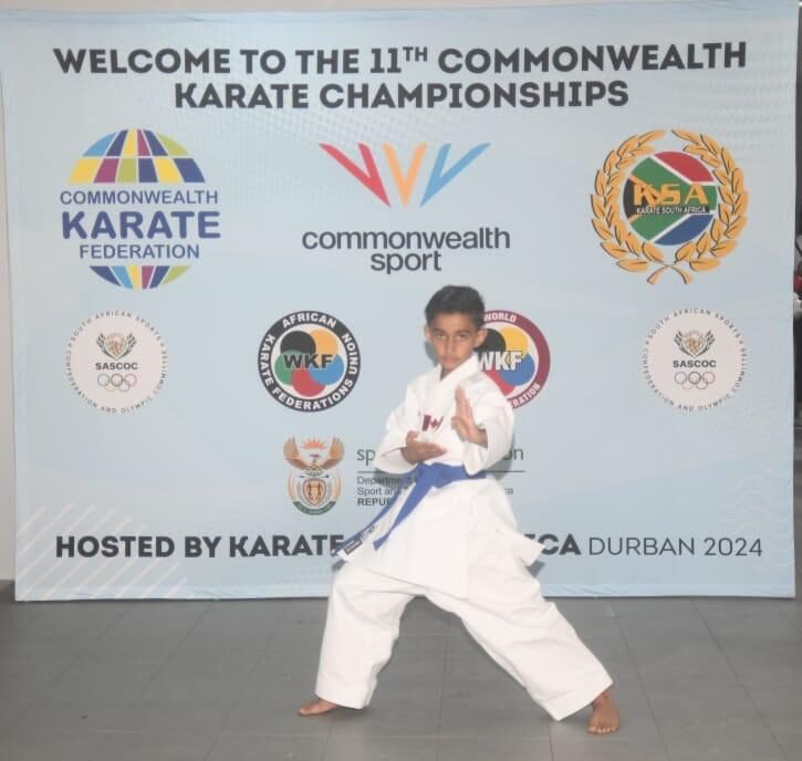 A young karate student wearing a blue belt and representing Canada poses proudly at the Commonwealth Sport event.