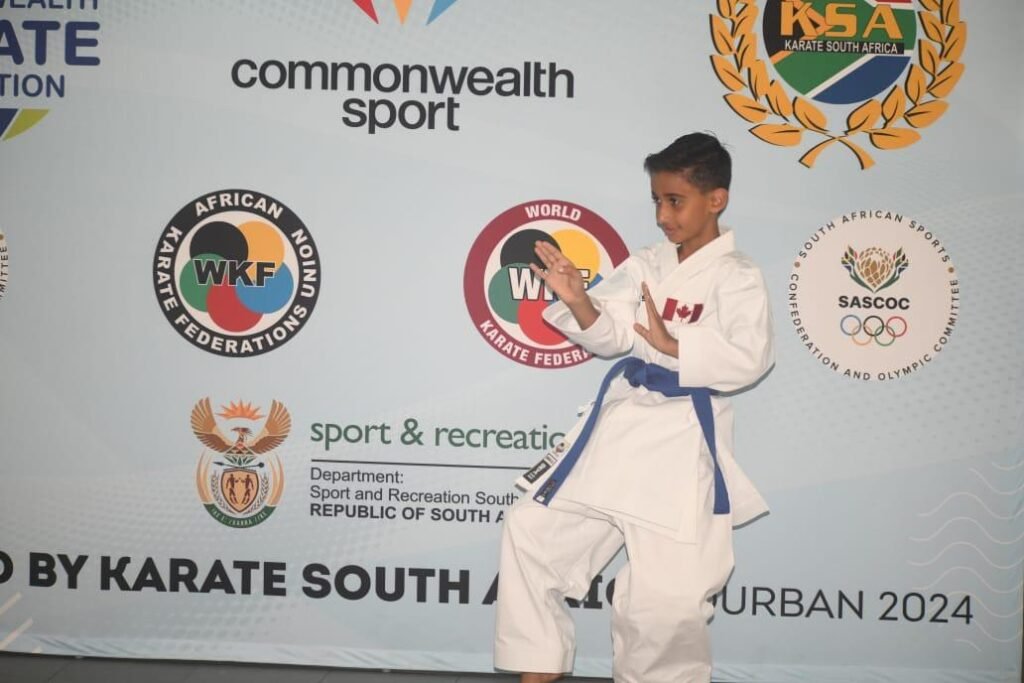 A young student from karate classes, proudly wearing a blue belt and representing Canada, poses at the Commonwealth Sport event.